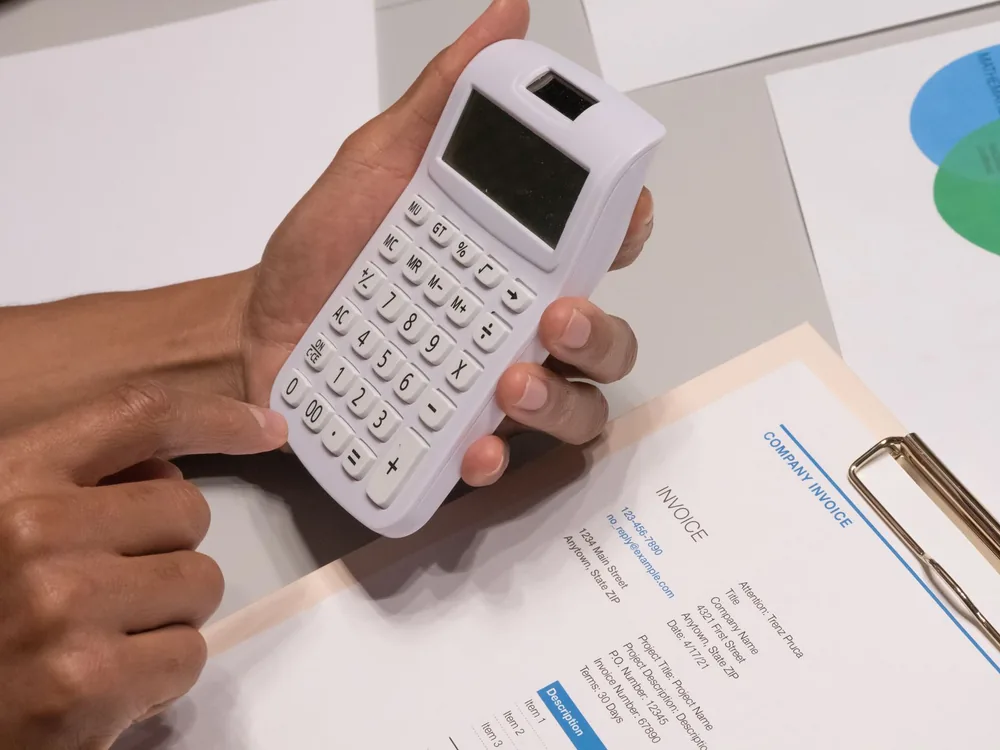 Mains tenant une calculatrice au-dessus d'une facture papier
