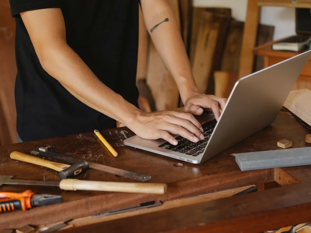 Artisan travaillant sur un ordinateur portable dans son atelier, entouré de ses outils